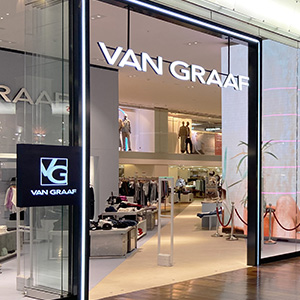 Eingang eines Van Graaf Modegeschäfts mit leuchtendem Logo und Blick ins Innere.