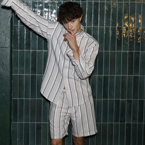 Ein Mann in einem gestreiften Pyjama-Set, bestehend aus einem Hemd und einer kurzen Hose, posiert vor einer grünen, gefliesten Wand.