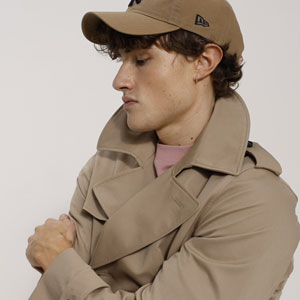 Ein Mann trägt einen beigen Trenchcoat und eine passende beige Baseballkappe.