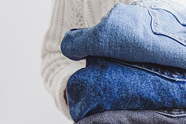 UnsereProdukte_CTA_teaser_Seitenabschluss Person holding a folded stack of blue denim jeans.