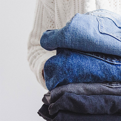 A person holding a stack of folded jeans and sweaters.