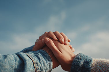 Two people clasping hands against a blue sky background.