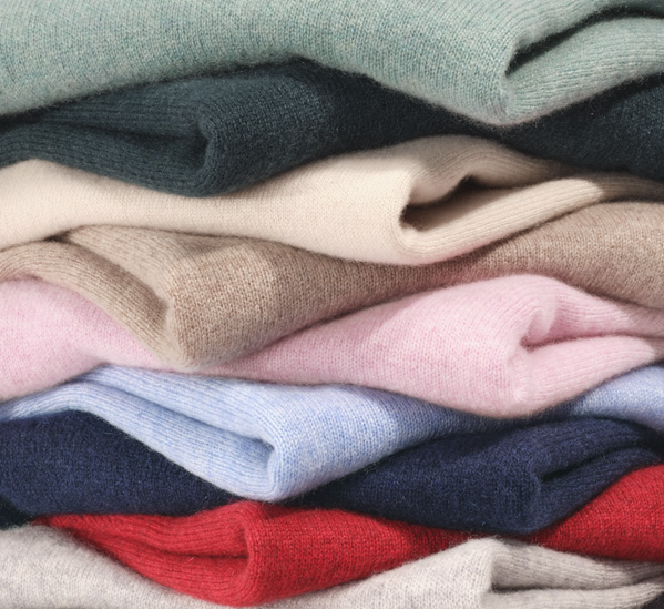 A stack of folded sweaters in various colours, including green, beige, pink, blue, and red.